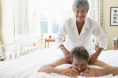 Woman giving man massage in bedroom smilingの写真素材