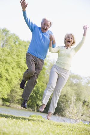 Couple jumping outdoors at park by lake smilingの写真素材