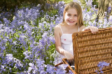 Young girl sitting outdoors with picnic basket smilingの写真素材