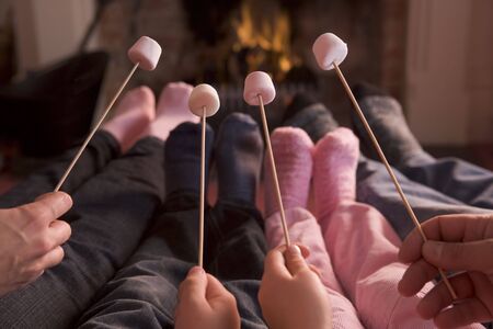 Feet warming at a fireplace with marshmallows on sticksの写真素材