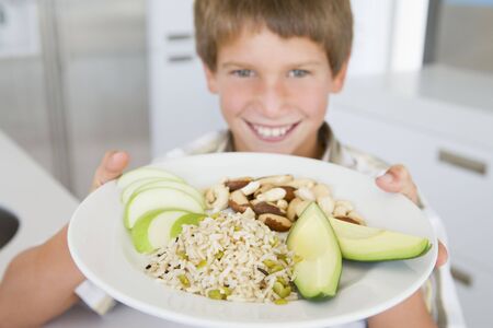 Young boy in kitchen eating rice fruit and nuts smilingの写真素材