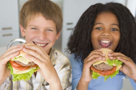 Two young children in kitchen eating cheeseburgers smilingの写真素材