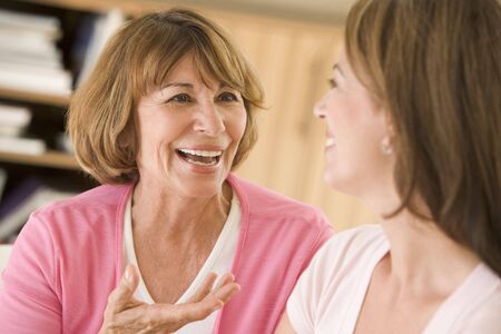 Two women sitting in living room talking and smilingの写真素材