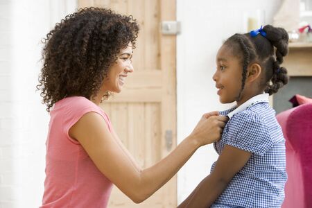 Woman in front hallway fixing young girl's dress and smilingの写真素材