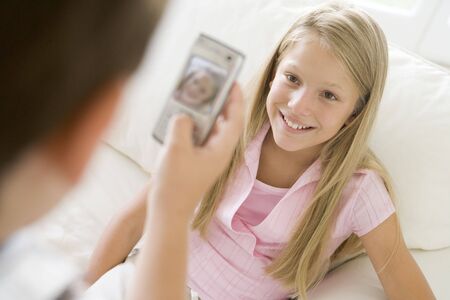Young boy taking picture of smiling young girl with camera phone indoorsの写真素材