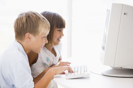 Two young children in home office with computer smiling