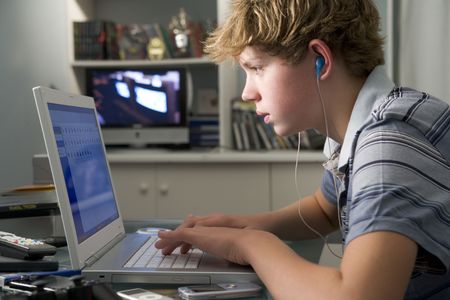 Young boy in bedroom using laptop and listening to MP3 player