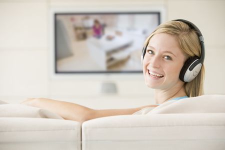 Woman in living room watching television and wearing headphones smiling