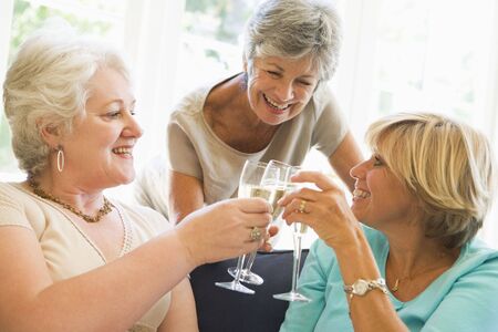 Three women in living room toasting champagne and smilingの写真素材