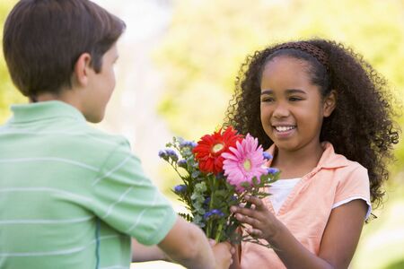 Young boy giving young girl flowers and smilingの写真素材