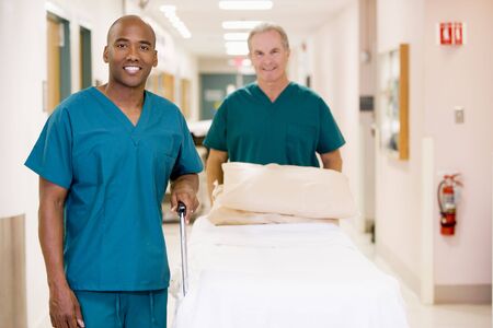 Two Orderlies Pushing An Empty Bed Down A Hospital Corridor