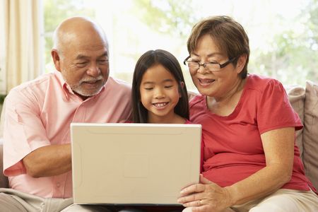 Grandparents And Grandaughter Using Laptop Computer At Homeの写真素材