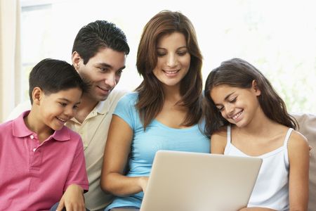 Family Sitting On Sofa At Home With Laptop