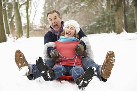Senior Couple Sledging Through Snowy Woodlandの写真素材