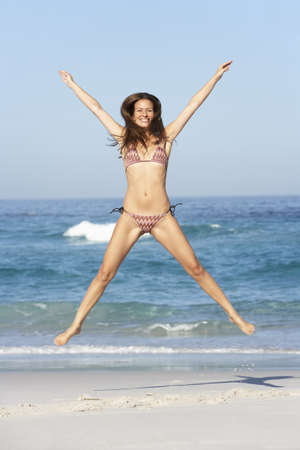 Athletic Young Woman Jumping On Sandy Beach On Holiday Wearing Bikiniの写真素材