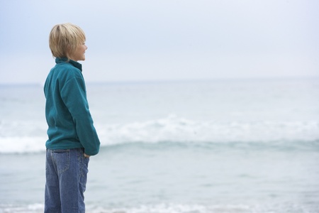 Young Boy On Holiday Standing On Winter Beach Looking Out To Seaの写真素材