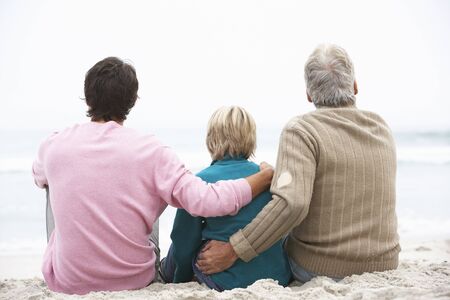 Grandfather, Father And Grandson Sitting On Winter Beach