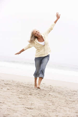Senior Woman On Holiday Running Along Winter Beachの写真素材