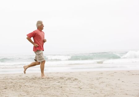 Senior Man On Holiday Running Along Winter Beachの写真素材
