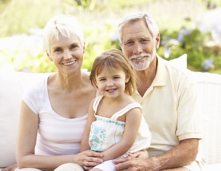 Grandparents And Granddaughter Relaxing In Garden
