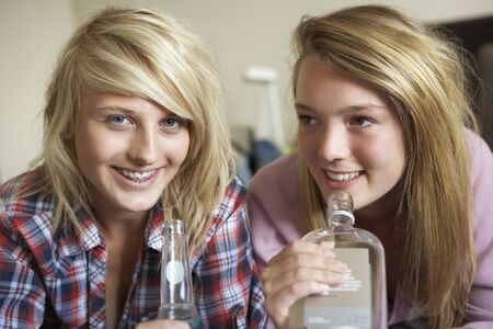 Two Teenage Girls Sitting On Sofa At Home Drinking Alcoholの写真素材
