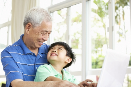 Chinese Grandfather And Grandson Sitting At Desk Using Laptop At Homeの写真素材
