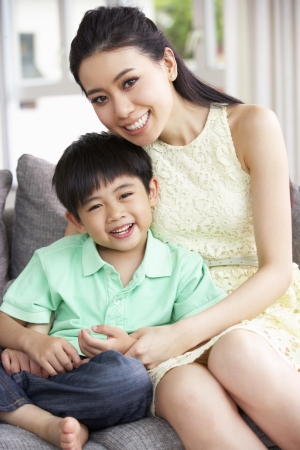 Chinese Mother And Son Sitting On Sofa At Home Togetherの写真素材