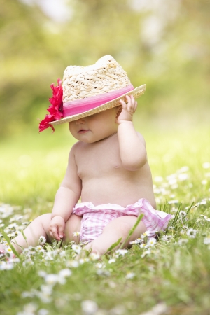 Baby Girl In Summer Dress Sitting In Field Wearing Straw Hatの写真素材