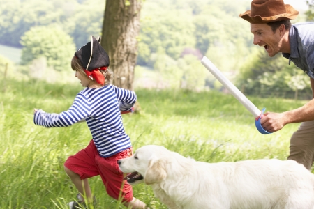 Father Playing Exciting Adventure Game With Son And Dog In Summer Fieldの写真素材