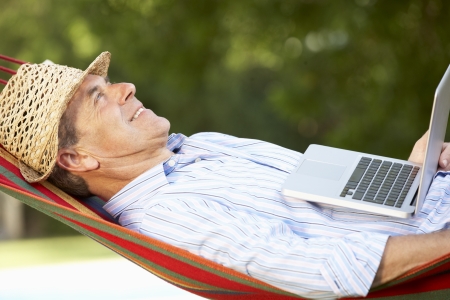 Senior Man Relaxing In Hammock With Laptopの写真素材