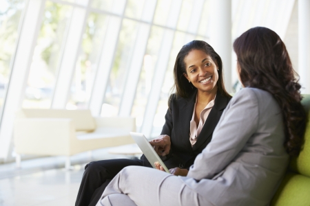 Businesswomen With Digital Tablet Sitting In Modern Officeの写真素材