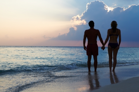 Silhouette Of Couple Walking Along Beach At Sunsetの写真素材