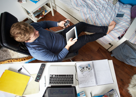 Teenage Boy Using Digital Tablet And Mobile Phone In Bedroomの写真素材