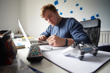 Teenage Boy Studying In Bedroom Using Laptop