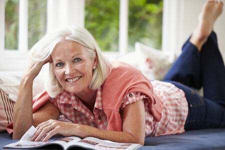 Middle Aged Woman Reading Magazine Lying On Sofaの写真素材