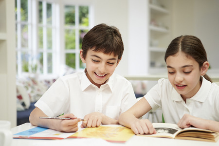 Children Wearing School Uniform Doing Homework In Kitchenの写真素材