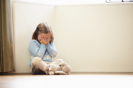 Unhappy Child Sitting On Floor In Corner At Homeの写真素材