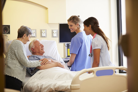 Medical Team Meeting With Senior Couple In Hospital Roomの写真素材