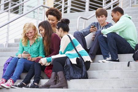 High School Students Sitting Outside Building With Phonesの写真素材