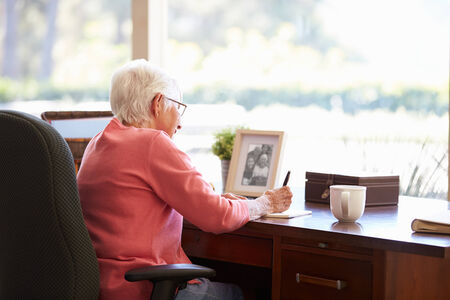 Senior Woman Writing Memoirs In Book At Deskの写真素材