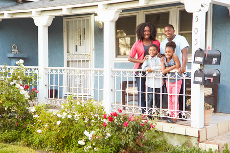 Portrait Of Family Standing On Porch Of Suburban Homeの写真素材