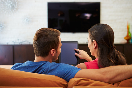Rear View Of Couple Sitting On Sofa Using Digital Tabletの写真素材