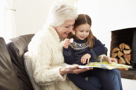 Grandmother And Granddaughter Reading Book At Home Togetherの写真素材