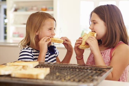Two Girls Eating Cheese On Toast In Kitchenの写真素材