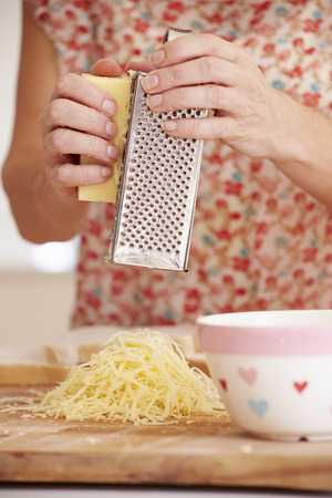Close Up Of Woman Grating Cheese In Kitchenの写真素材