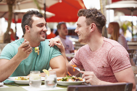 Male Couple Enjoying Lunch In Outdoor Restaurantの写真素材