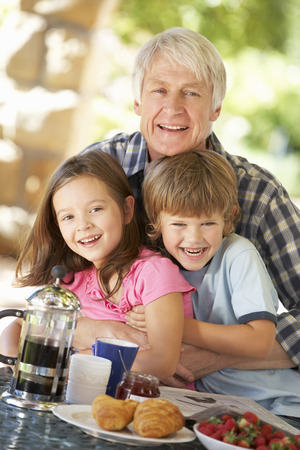 Mid age man and grandchildren eating breakfast outdoorsの写真素材