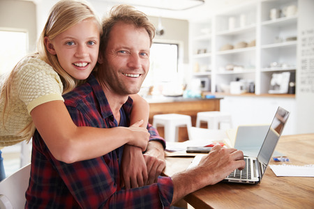 Girl hugging her father, working on laptop at homeの写真素材