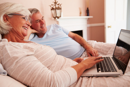 Senior Couple Lying In Bed Looking At Laptop Computer