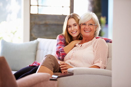 Grandmother With Adult Granddaughter Relaxing On Sofaの写真素材